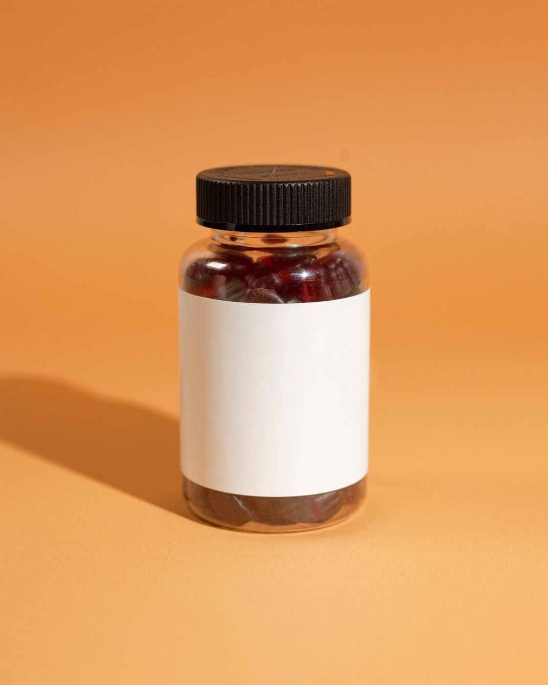 Frasco de cápsulas com rótulo em branco, sobre fundo laranja liso