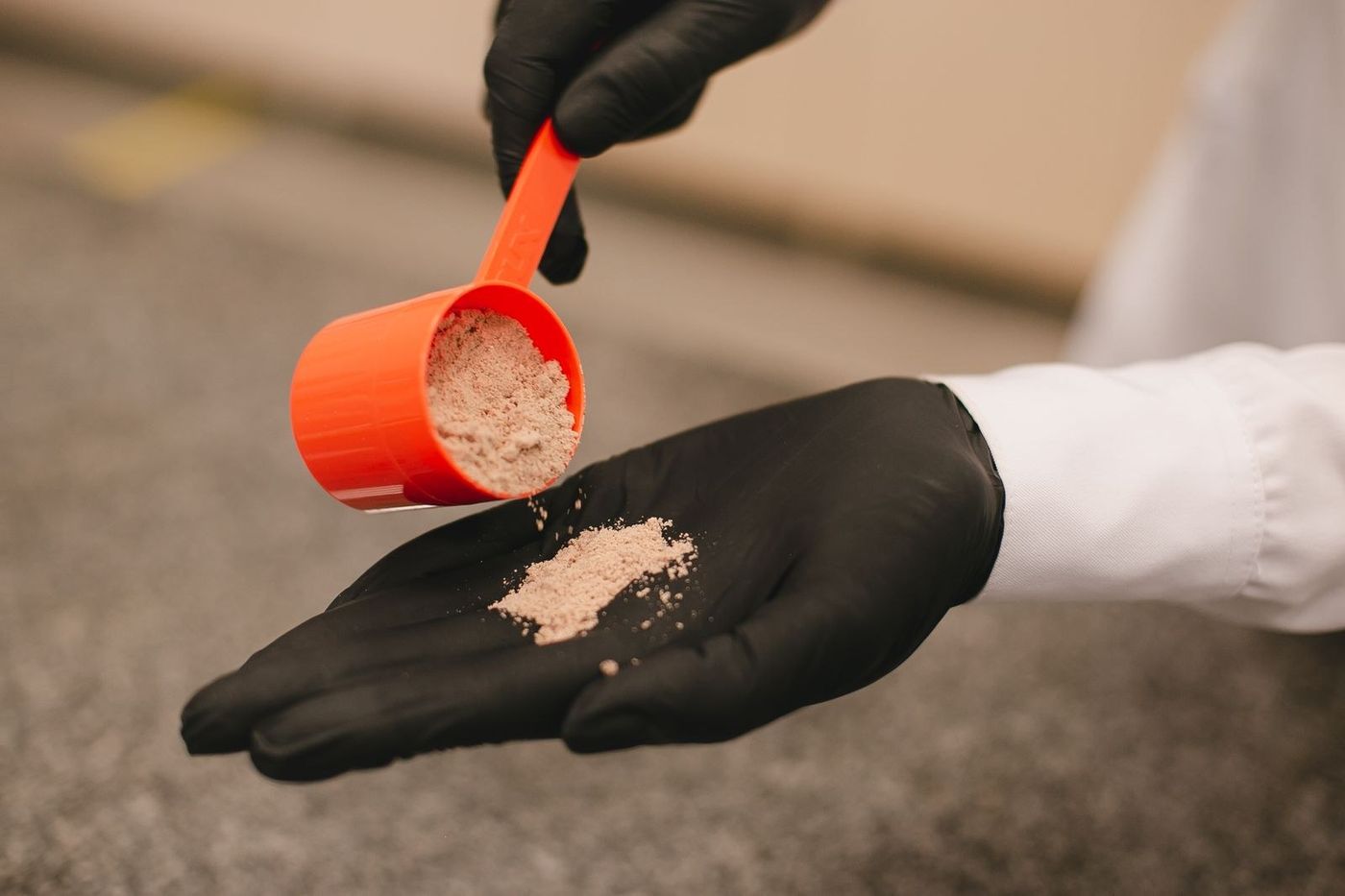 Mão de luva preta despejando um dosador de pó na palma